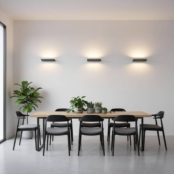 Black internal wall uplighters o a grey wall with a table and chairs and plants in the room