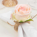 Rose napkin ring decoration with twine on a white table setting.