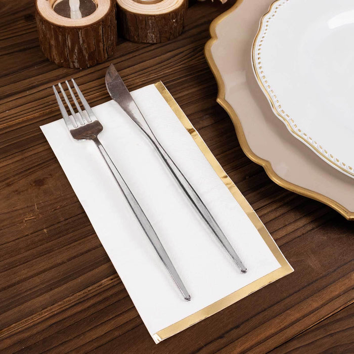Silver fork and knife on a napkin with gold trim on a wooden table.