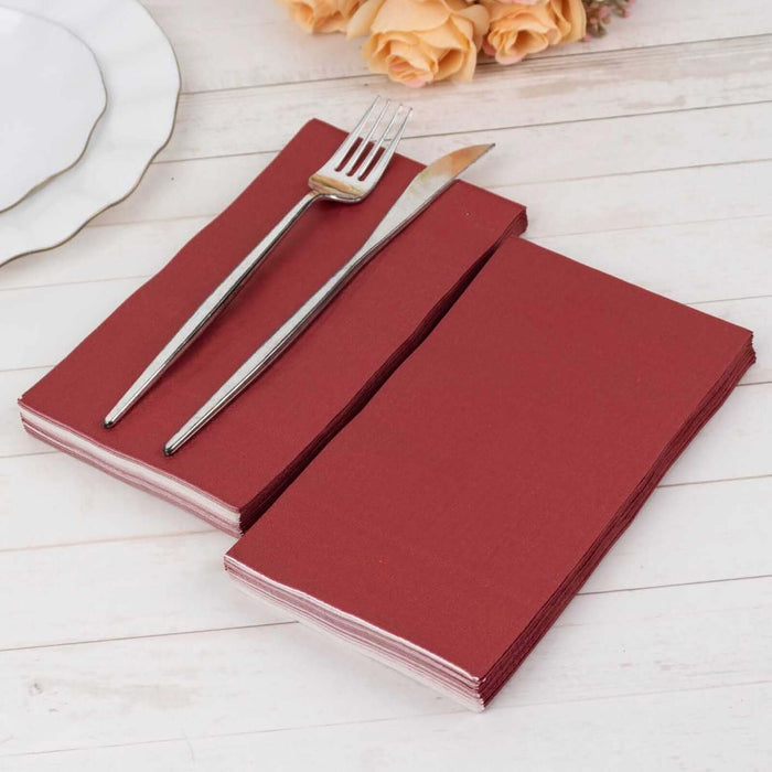 Burgundy napkins with a fork and knife on a rustic wooden table.