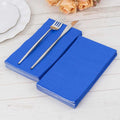 Blue paper napkins stacked with a fork and knife on a wooden table.