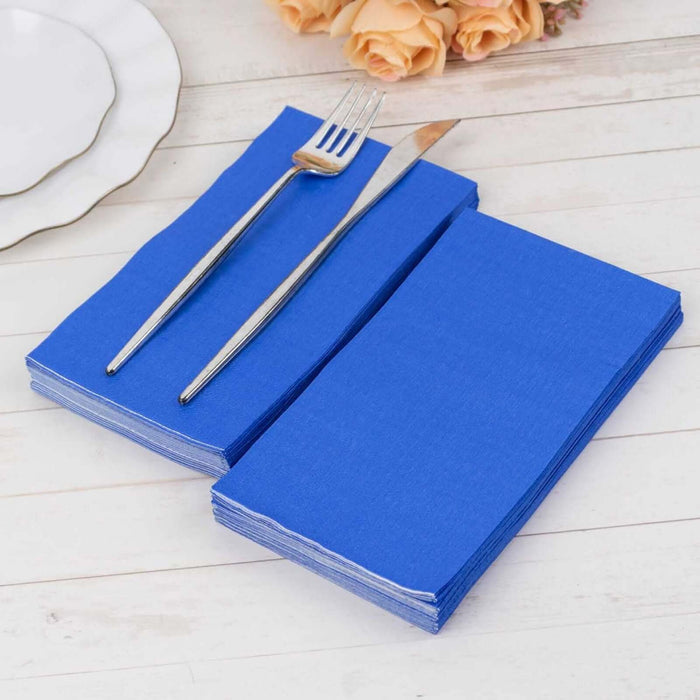 Blue paper napkins stacked with a fork and knife on a wooden table.