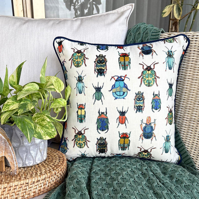 Decorative pillow with a colorful beetle print, surrounded by greenery and cozy green throw.