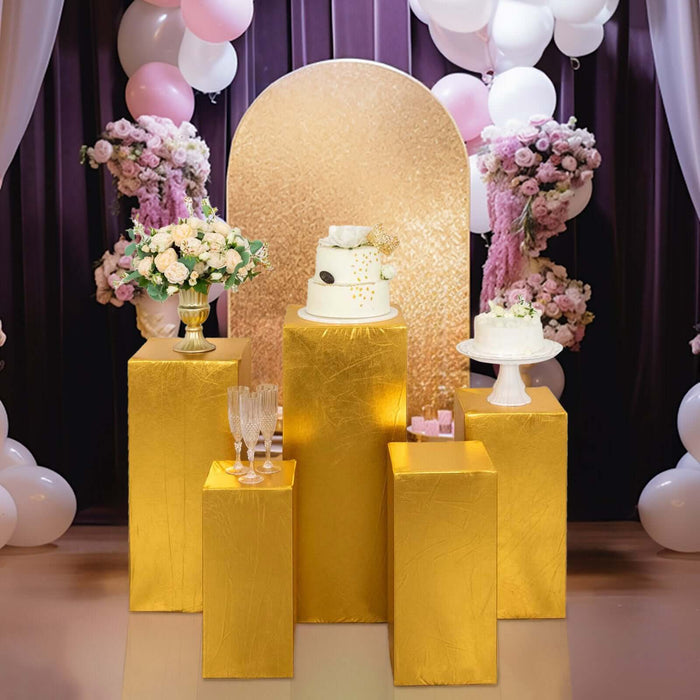 Elegant gold display tables with wedding cakes and floral arrangements at a celebration scene.